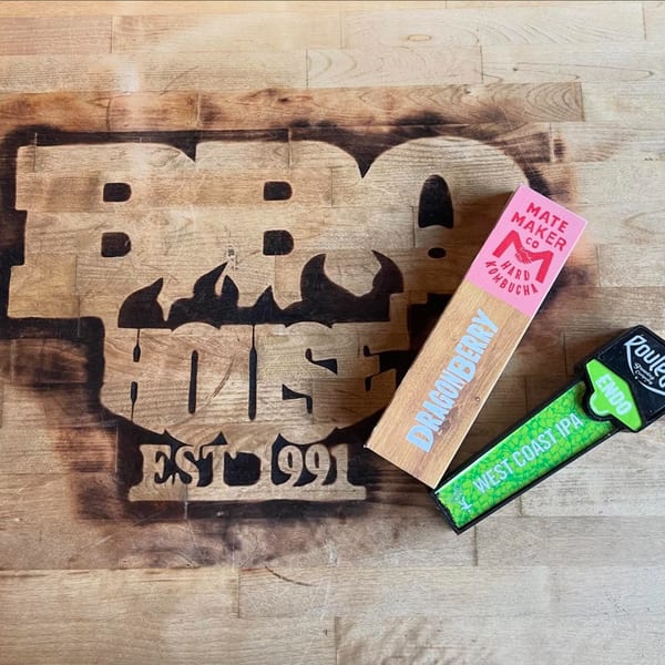 Burnt wood BBQ House logo with Dragonberry Hard Kombucha and West Coast IPA tap handles.