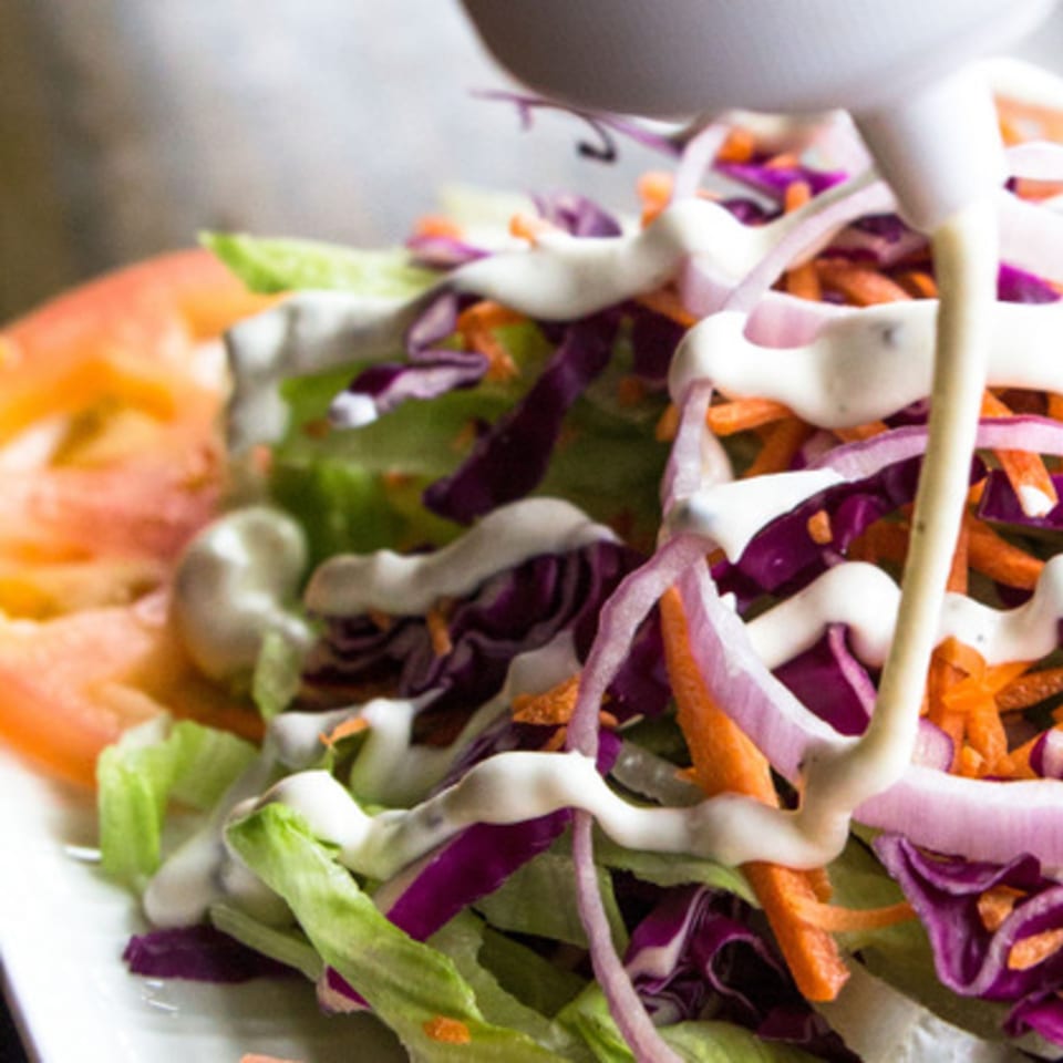 Creamy dressing drizzled over a fresh salad with lettuce, red cabbage, carrots, and red onion.