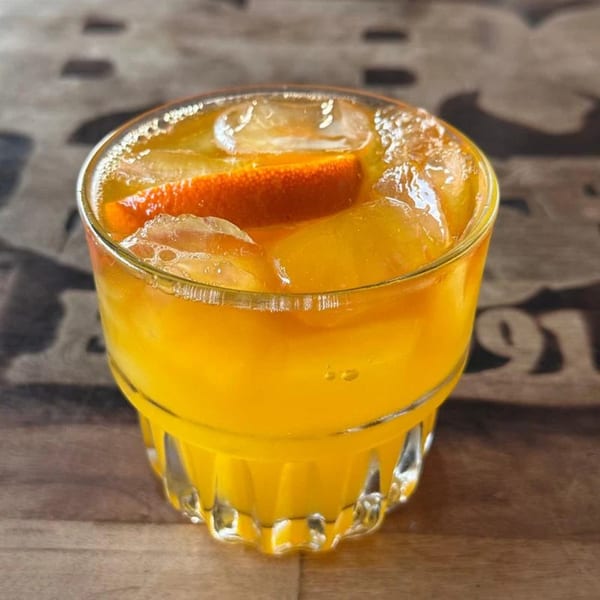 A vibrant orange cocktail with ice and an orange slice sits on a wooden table.