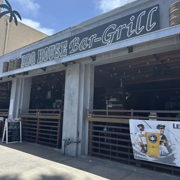 Exterior of BBQ House Bar & Grill, a concrete building with a large sign and outdoor seating.
