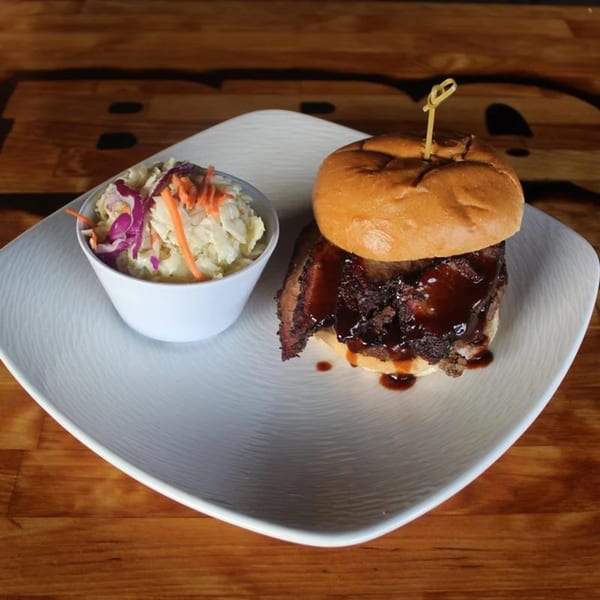 BBQ House Bar & Grill's brisket sandwich with BBQ sauce and a side of coleslaw on a white plate.