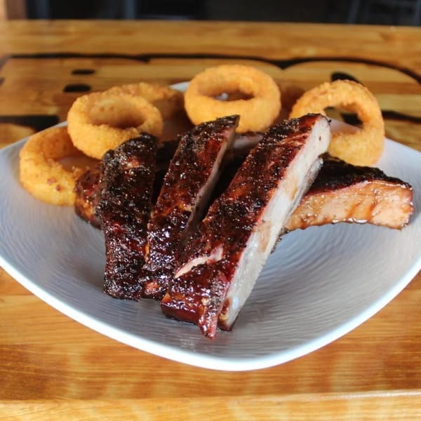 BBQ House Bar & Grill's BBQ ribs with a side of crispy onion rings on a white plate.