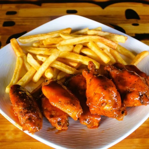A white plate with BBQ House Bar & Grill's buffalo wings and a side of golden french fries.