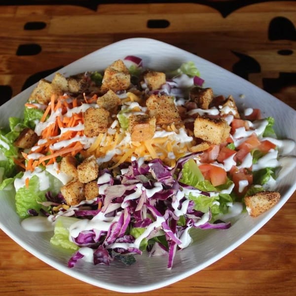 A BBQ House Bar & Grill salad with lettuce, carrots, cheese, tomatoes, croutons, and dressing.